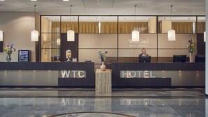 A reception desk at the WestCord WTC Hotel with a modern design, including a glass partition, a minibar, and a vase with flowers. - Westcord WTC Hotel Leeuwarden (Leeuwarden)