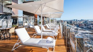 A deck with sun loungers and umbrellas, overlooking a cityscape.