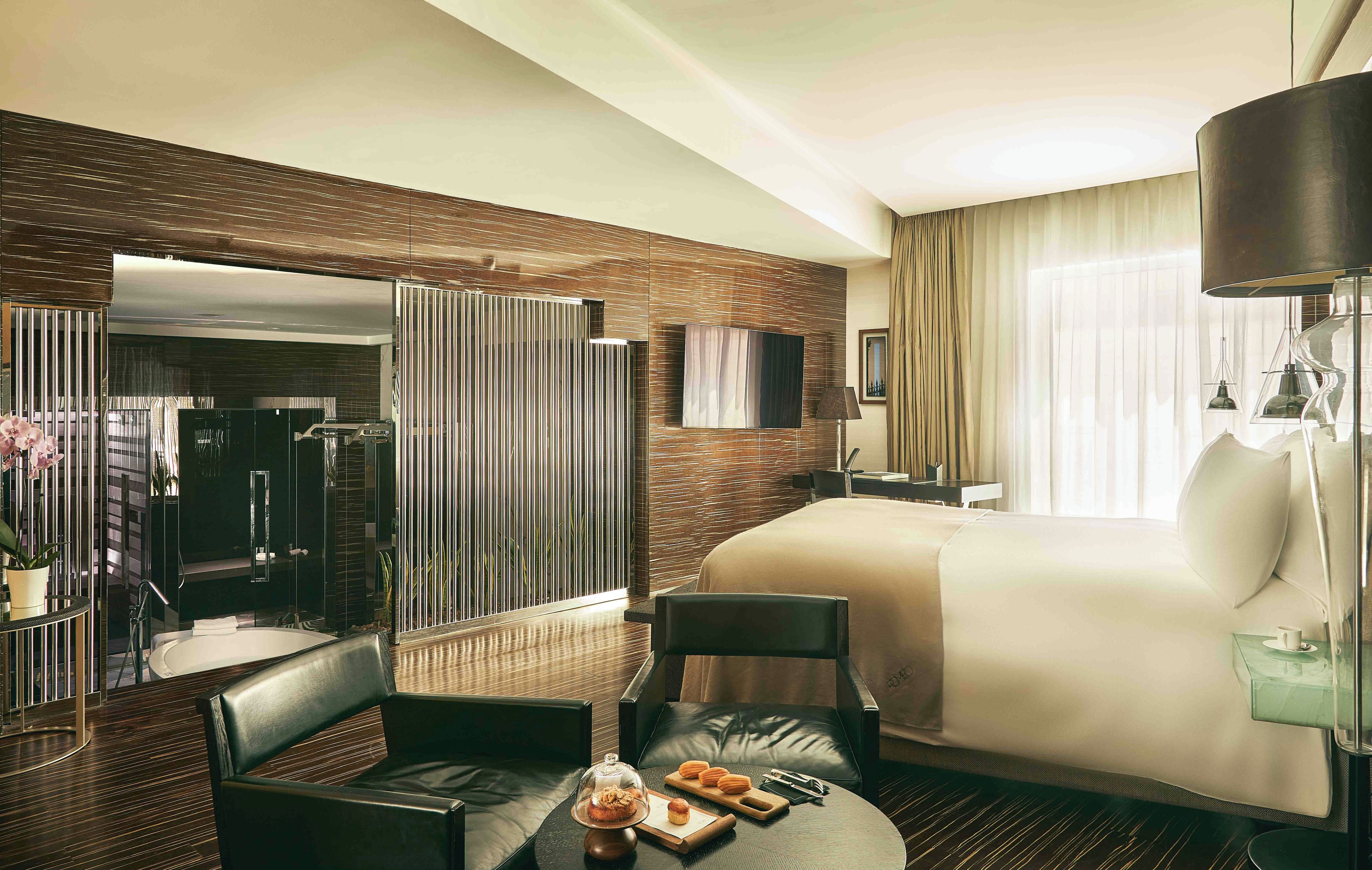 A hotel room with a large bed, a sitting area with a coffee table, a mirror, and a view of the hotel corridor.