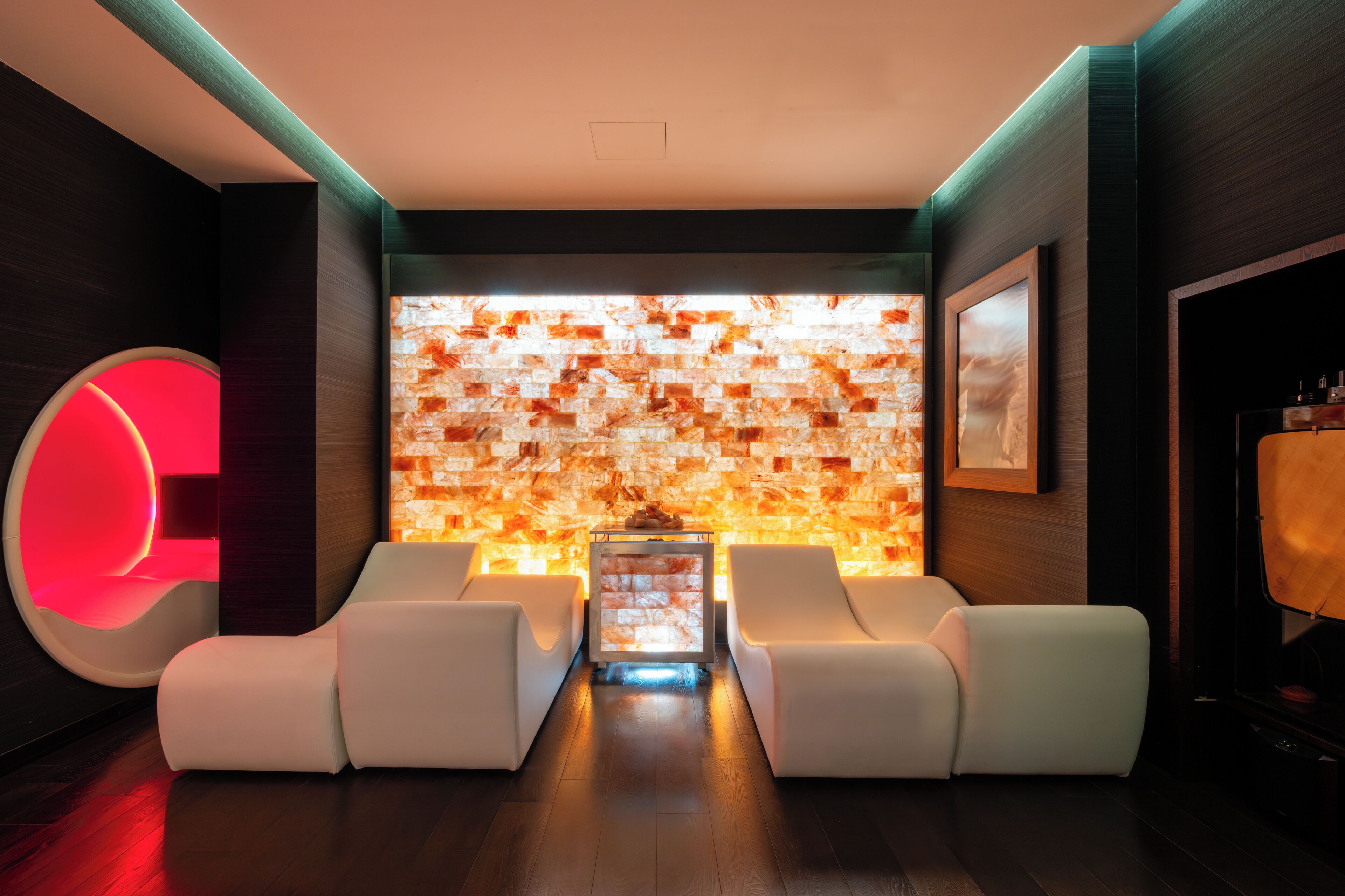 Un espace lounge moderne agrémenté d’un grand panneau lumineux en forme de « C », d’une cheminée et de canapés en cuir blanc.
