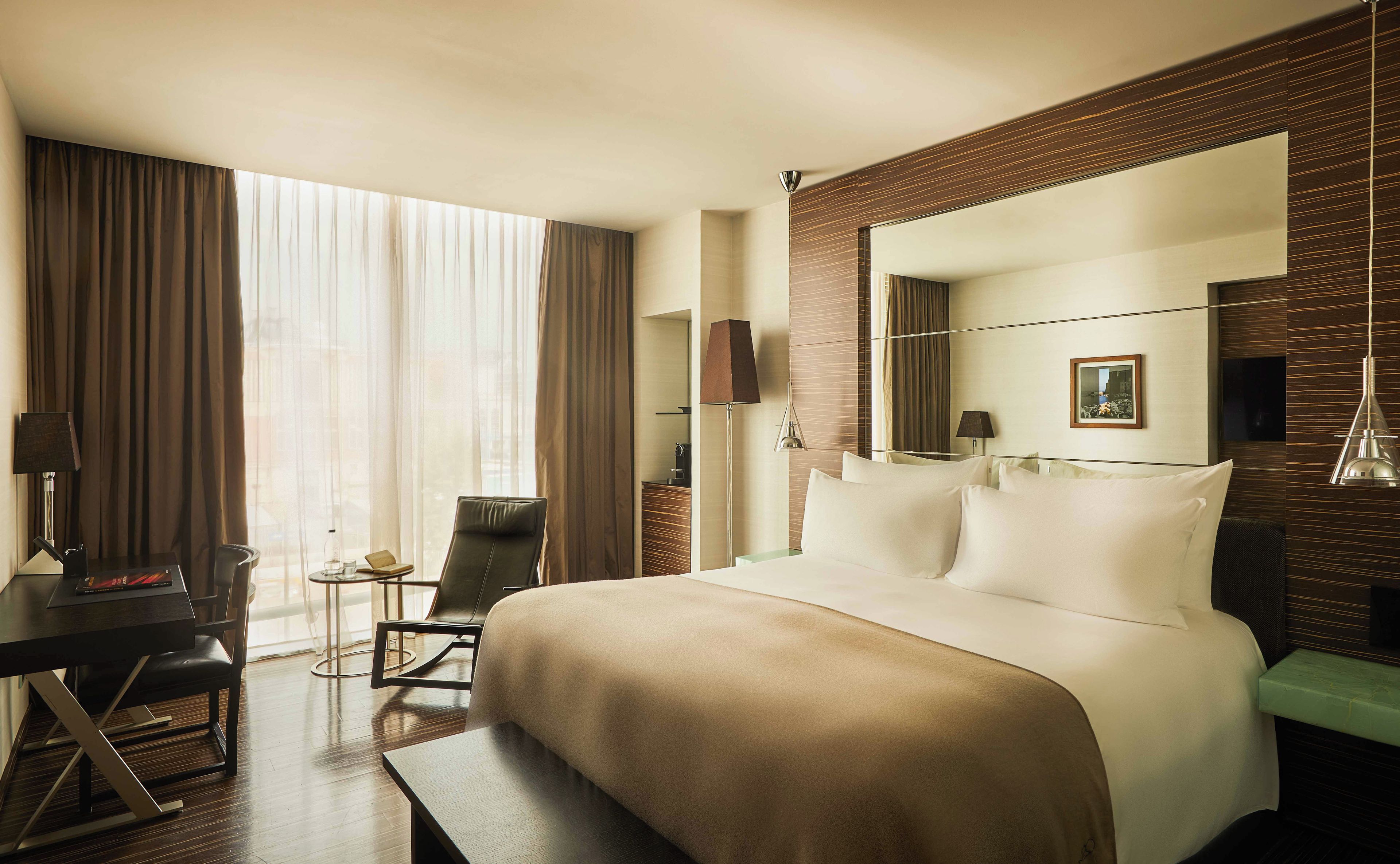 A hotel room with a large bed, a desk, a chair, and a view of the city through the window.