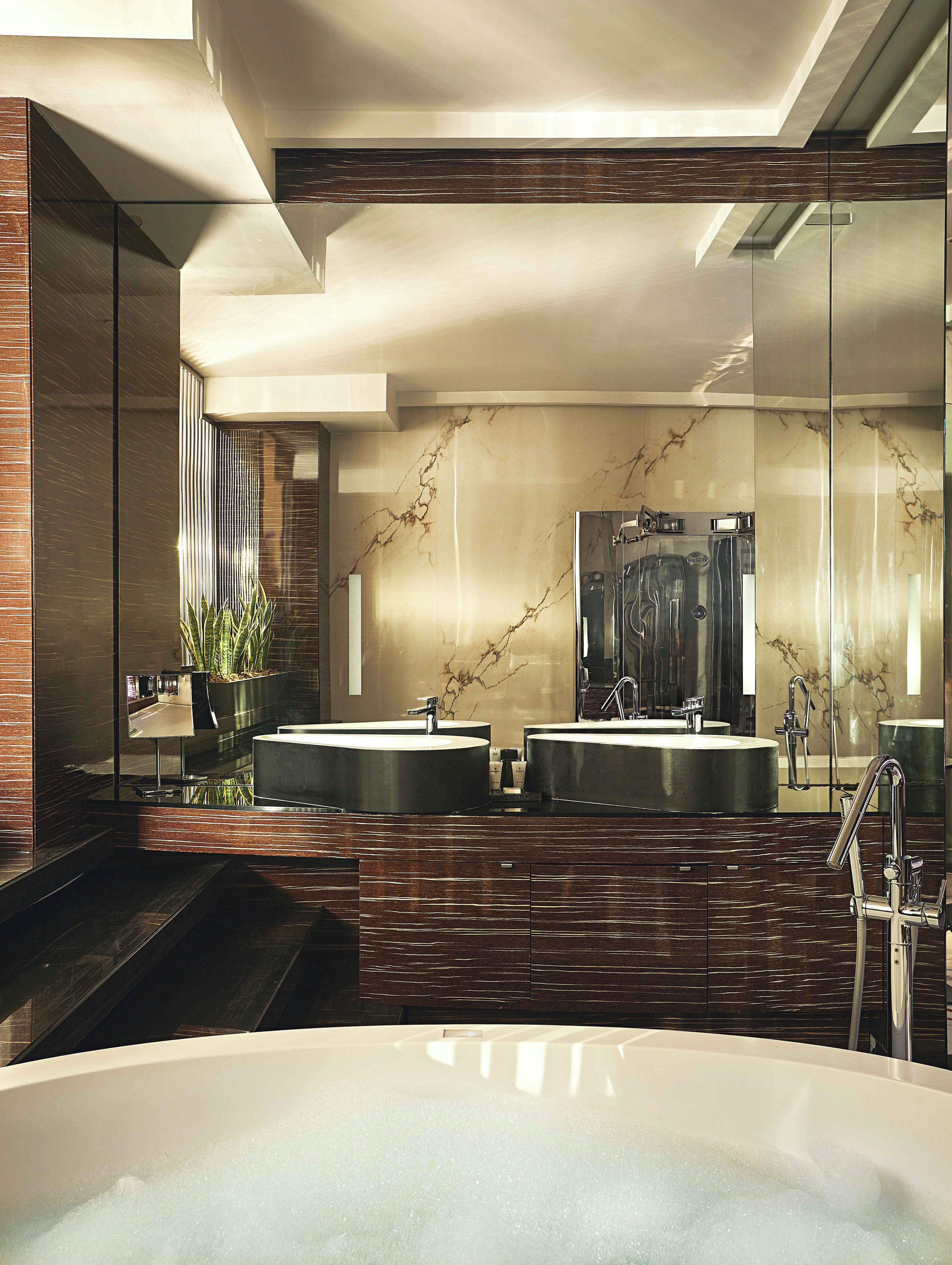 A modern bathroom with two sinks, a large mirror, and a bathtub.