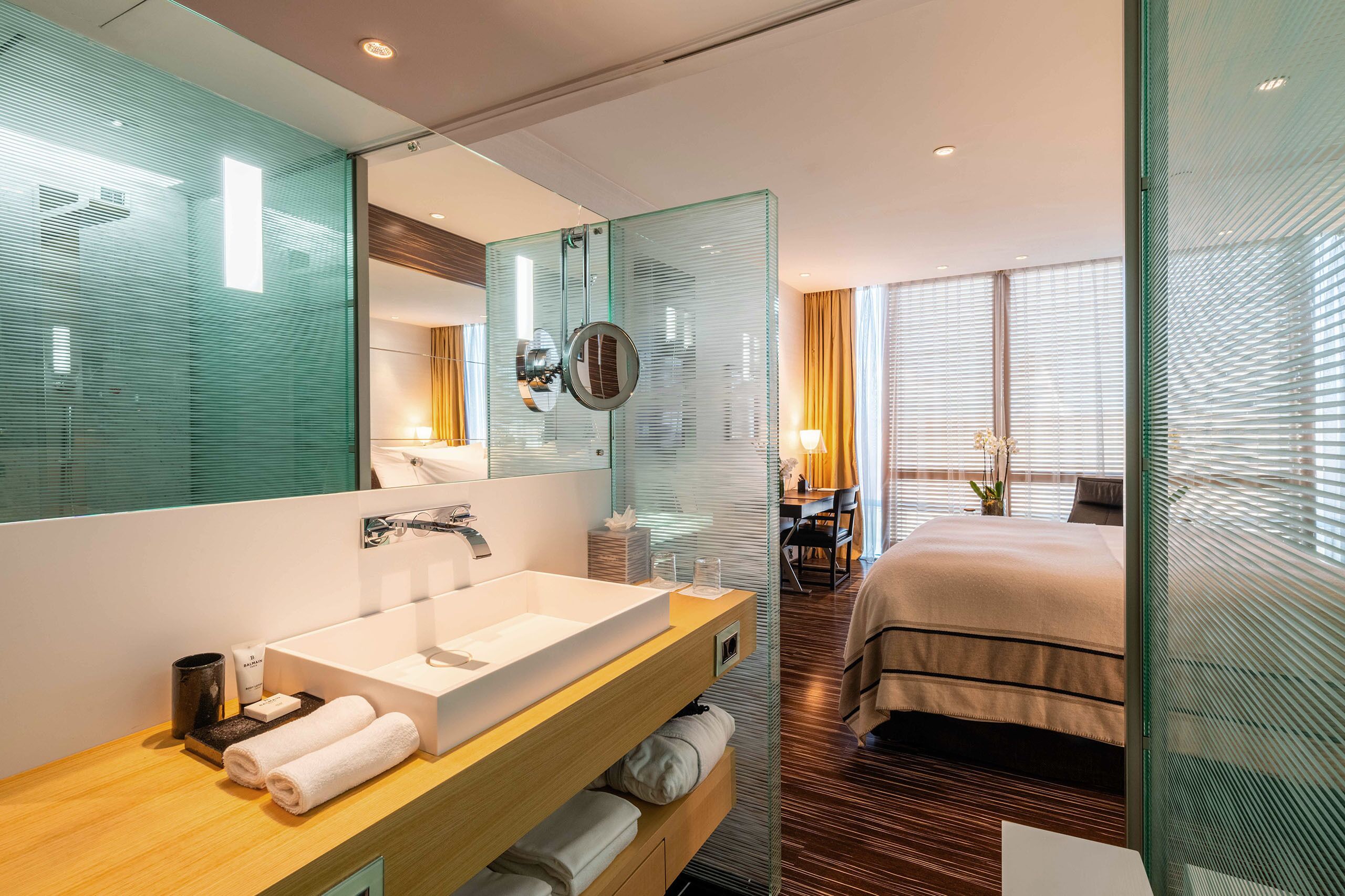 A modern hotel room with a large bathroom sink, a mirror, a bedside table, and a bed.