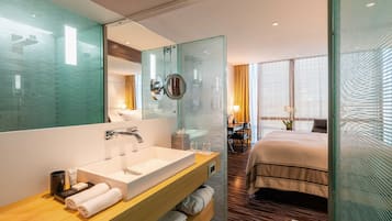 A modern hotel room with a large bathroom sink, a mirror, a bedside table, and a bed.