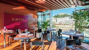 A modern restaurant with a view of a cityscape, featuring wooden flooring, glass tables, and a prominent Krug Champagne sign.