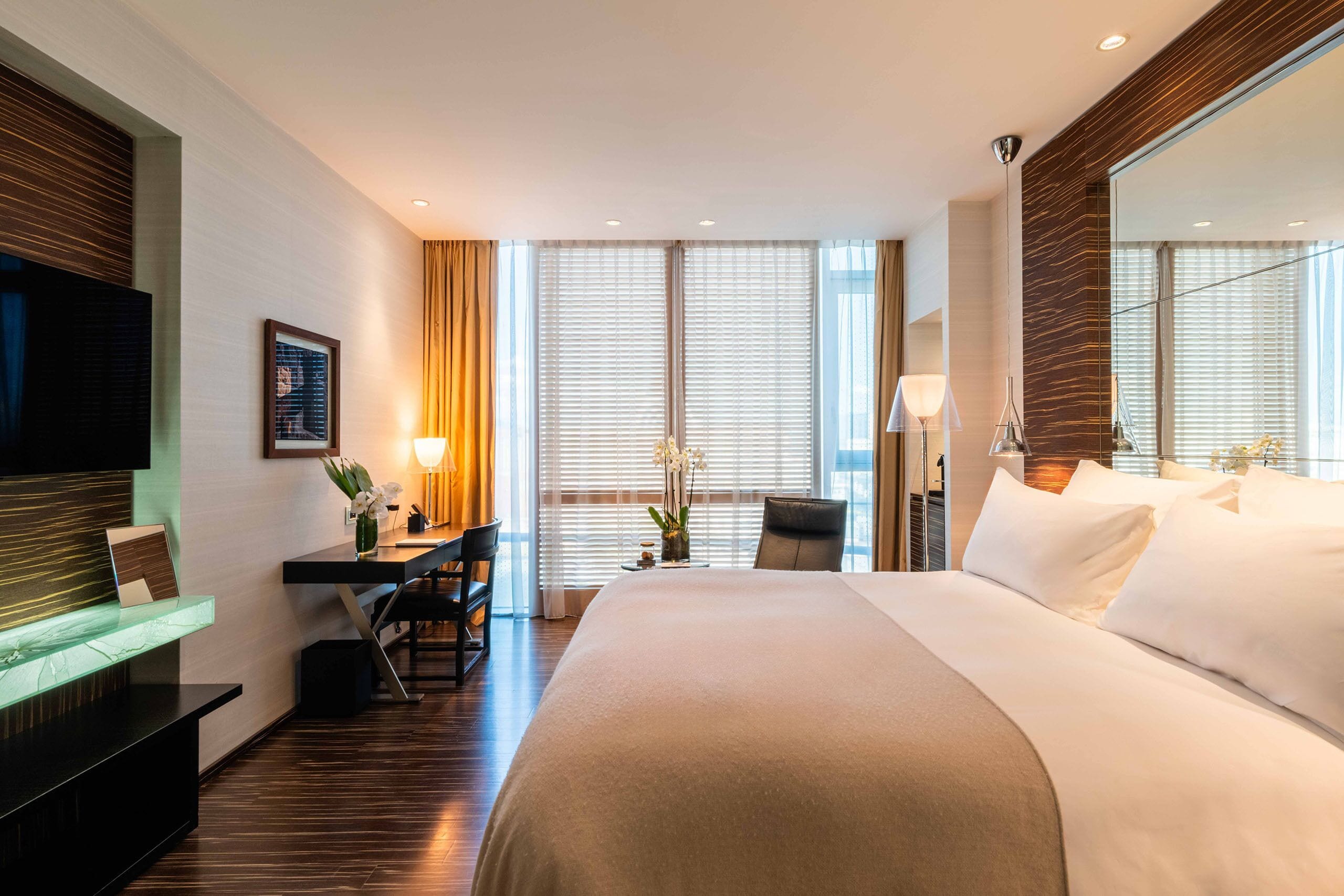 Habitación de hotel con una cama grande, un escritorio con una silla, un televisor y un espejo amplio.