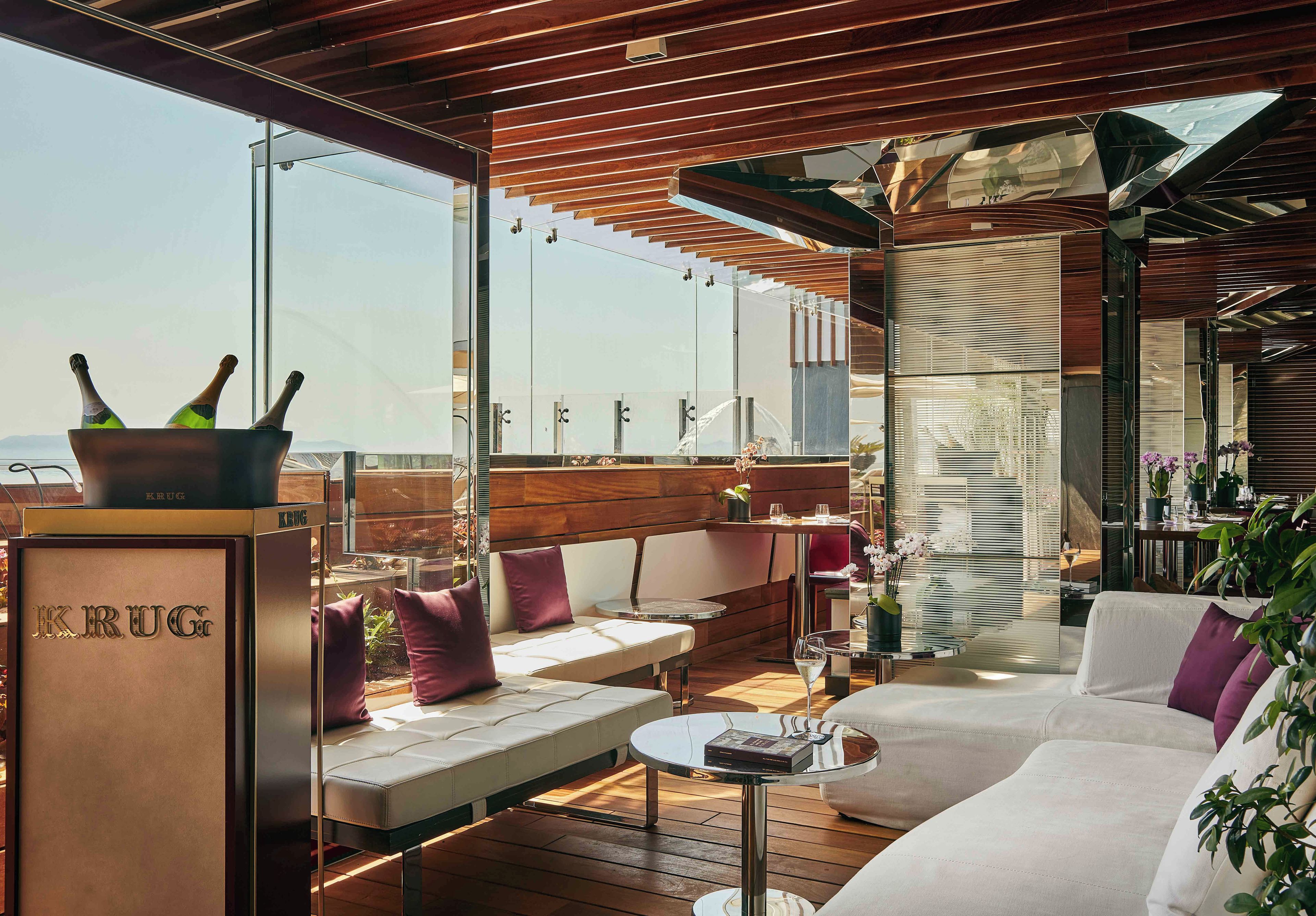 A modern outdoor seating area with a wooden ceiling, cushioned seating, and a glass table.