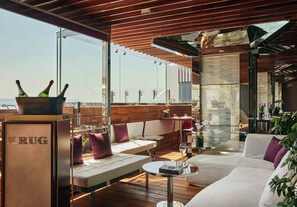 A modern outdoor seating area with a wooden ceiling, cushioned seating, and a glass table.