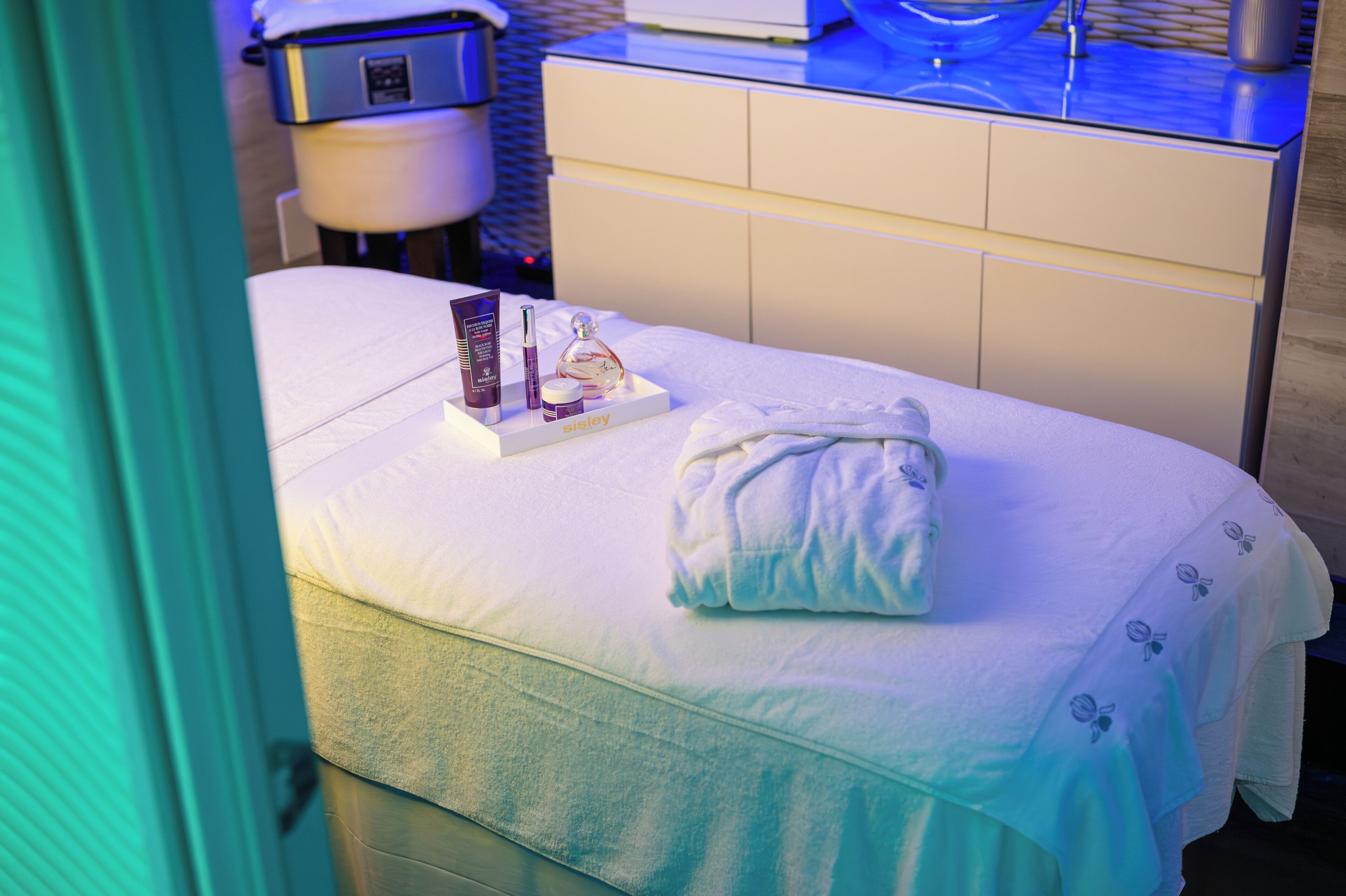 A neatly made bed with a white bedspread, a folded towel, and a toiletry set on a bedside table.