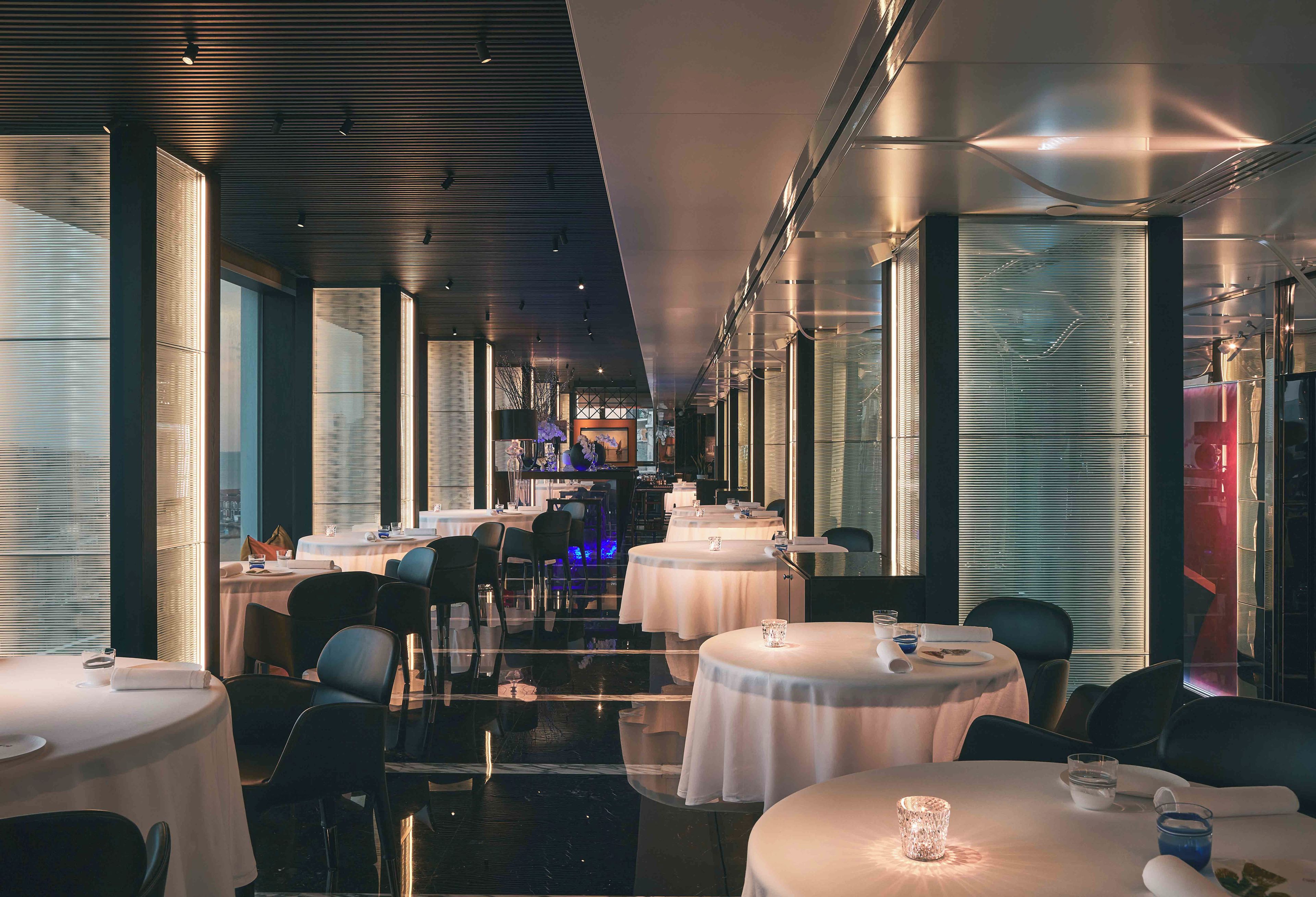 A modern restaurant with round tables, black chairs, and a glass partition wall.