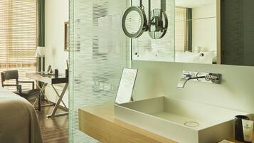 A modern bathroom with a glass partition, a large mirror, a wooden vanity, and a shower area.