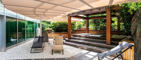 A covered outdoor area with a wooden pergola, seating, and a view of greenery.