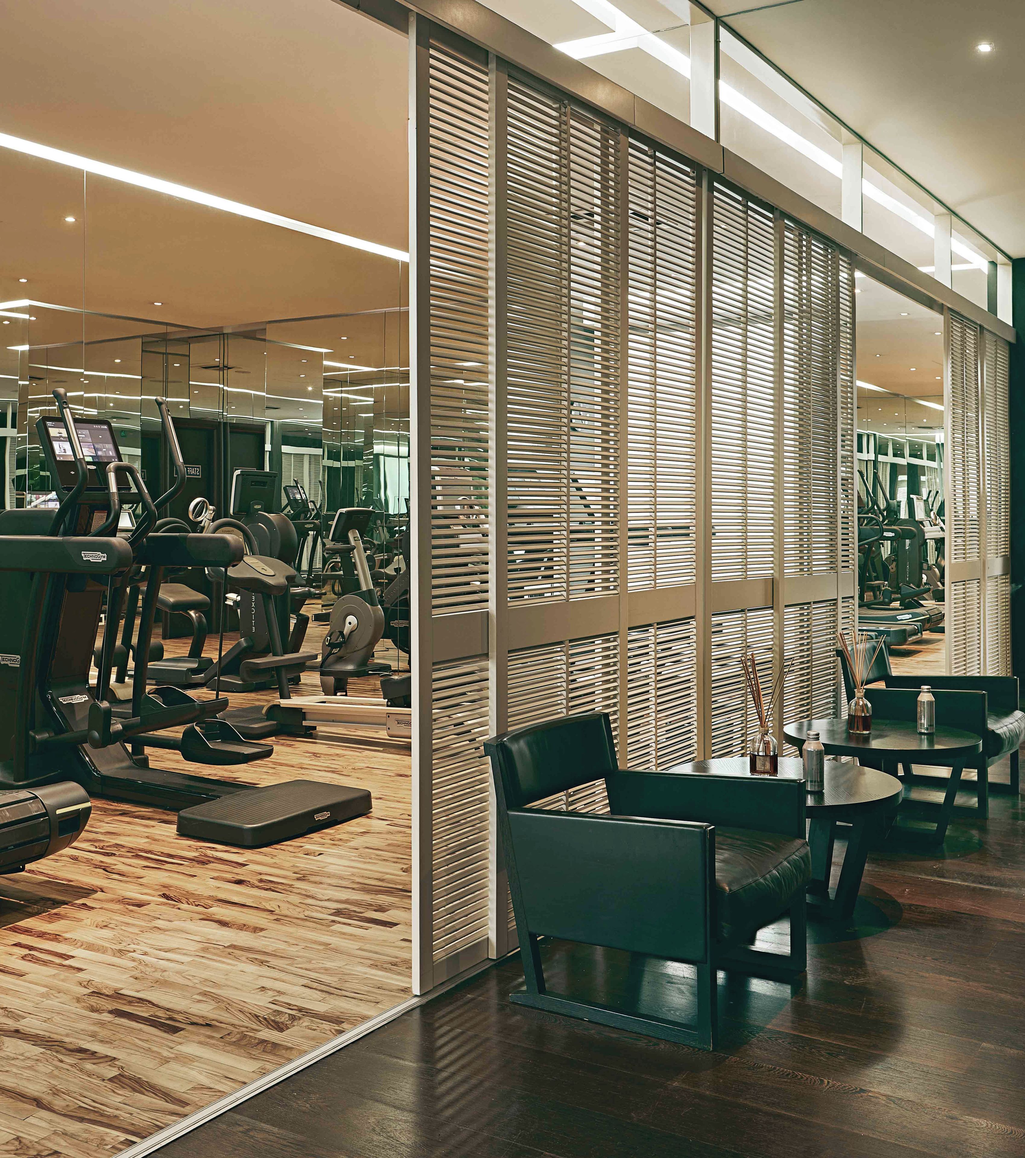 A modern gym with exercise equipment, a wooden floor, and a seating area with a table and chairs.