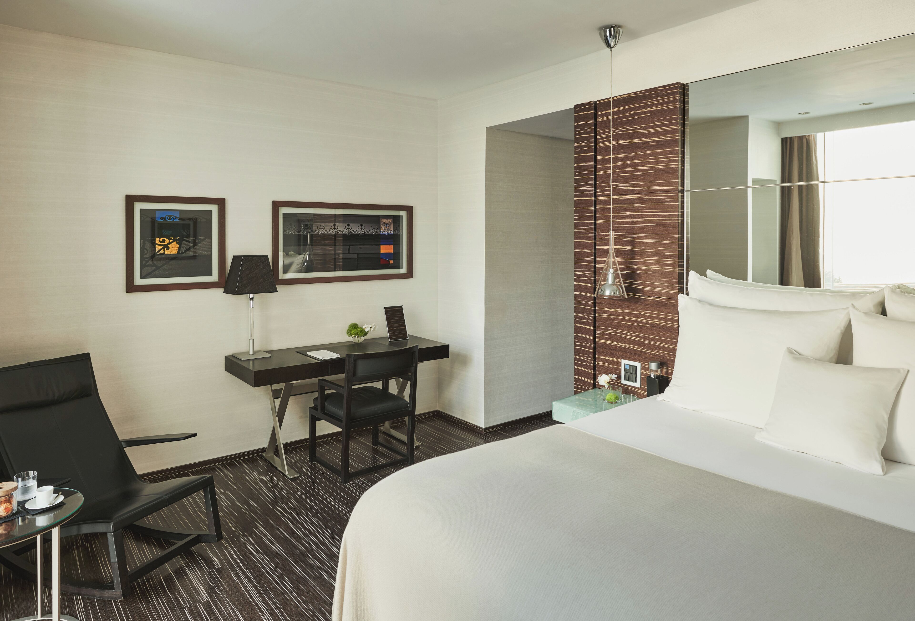 A hotel room with a bed, a desk, a chair, a lamp, and two framed pictures on the wall.