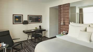 Habitación de hotel con cama, escritorio, silla, lámpara y dos cuadros en la pared.