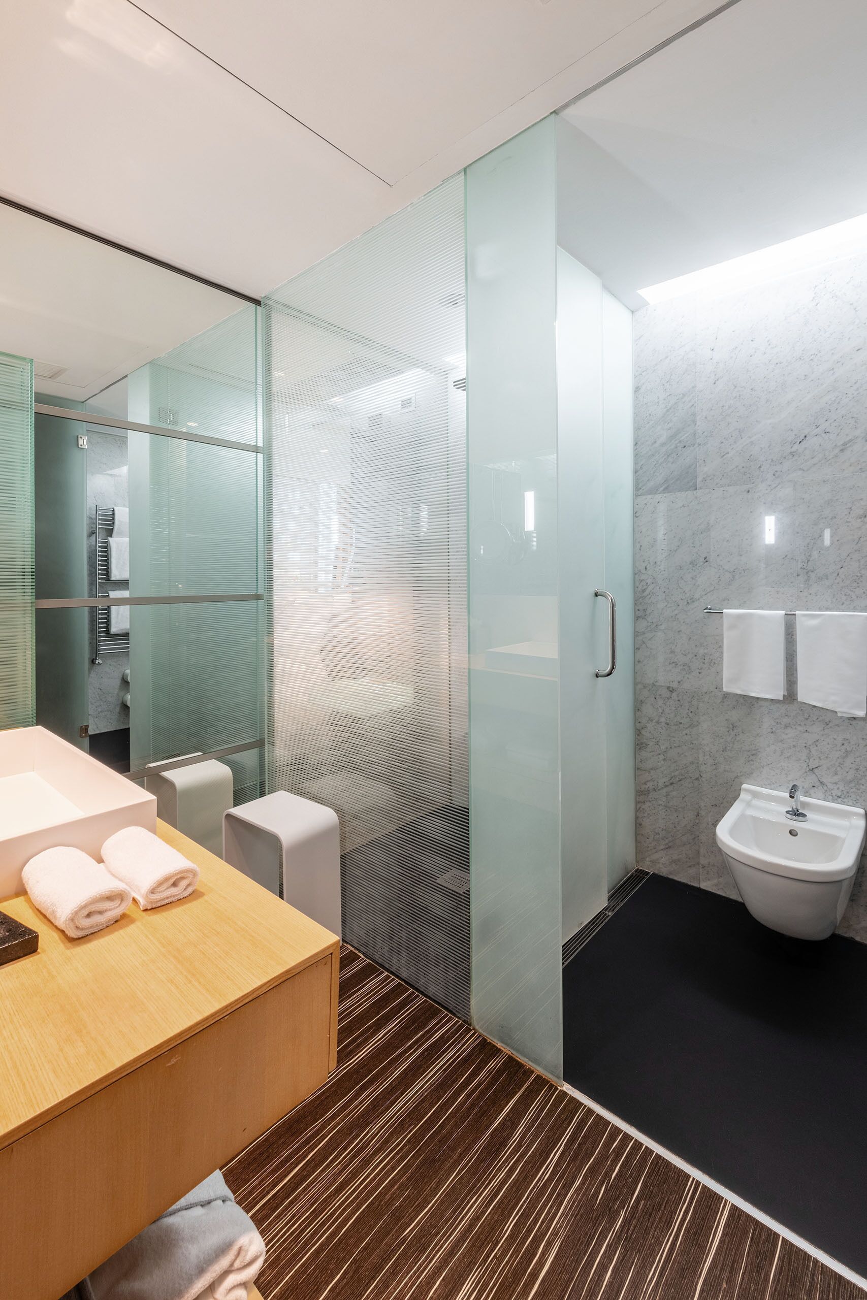 A modern bathroom with a glass shower enclosure, a wooden vanity with a sink, and a marble-tiled wall.