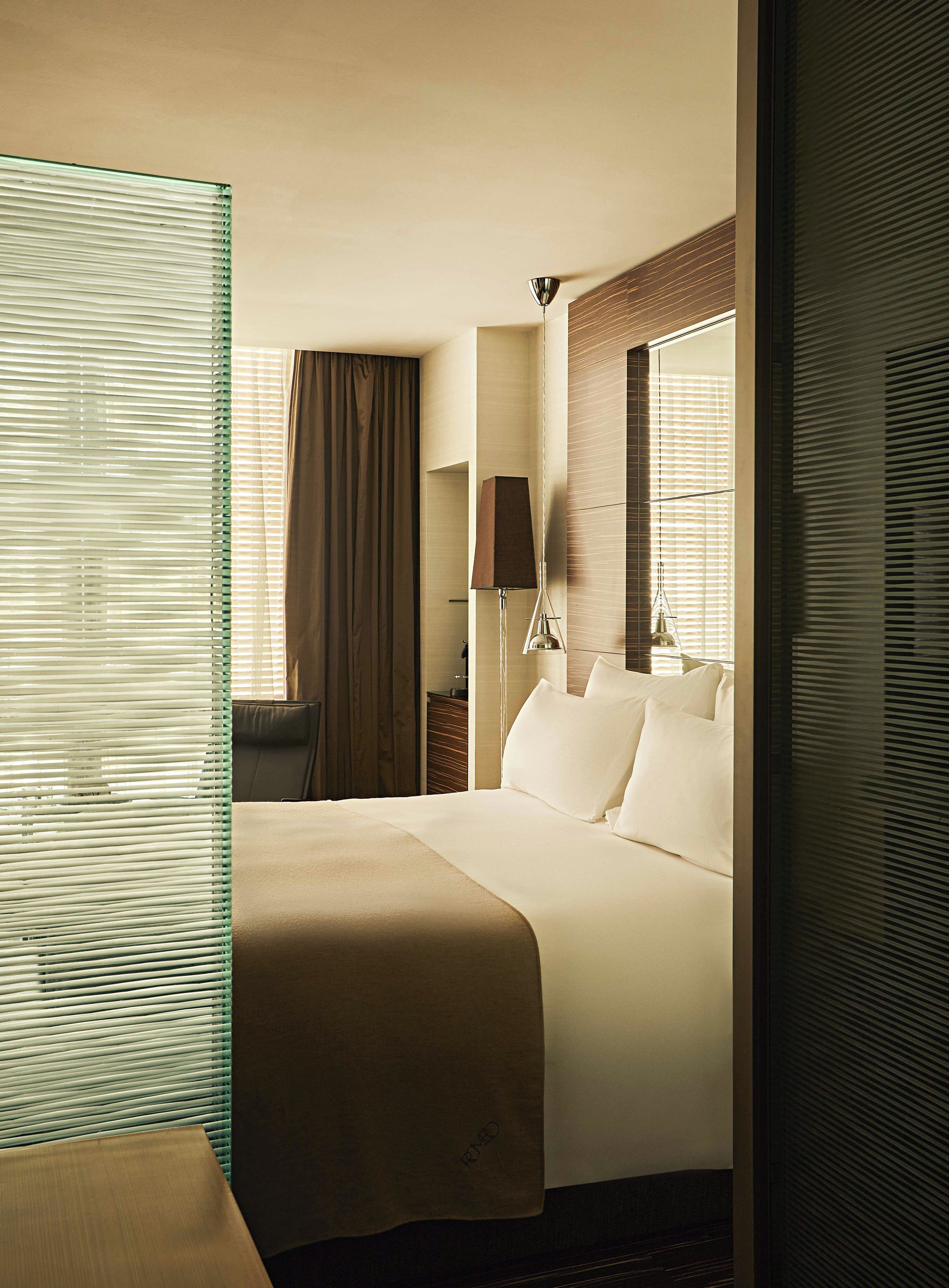 A hotel room with a large bed, a desk, a chair, a lamp, and a window with blinds.