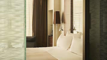 A hotel room with a large bed, a desk, a chair, a lamp, and a window with blinds.