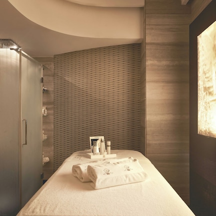 A hotel room with a bed, a vanity with a mirror, and a wall with a textured pattern.