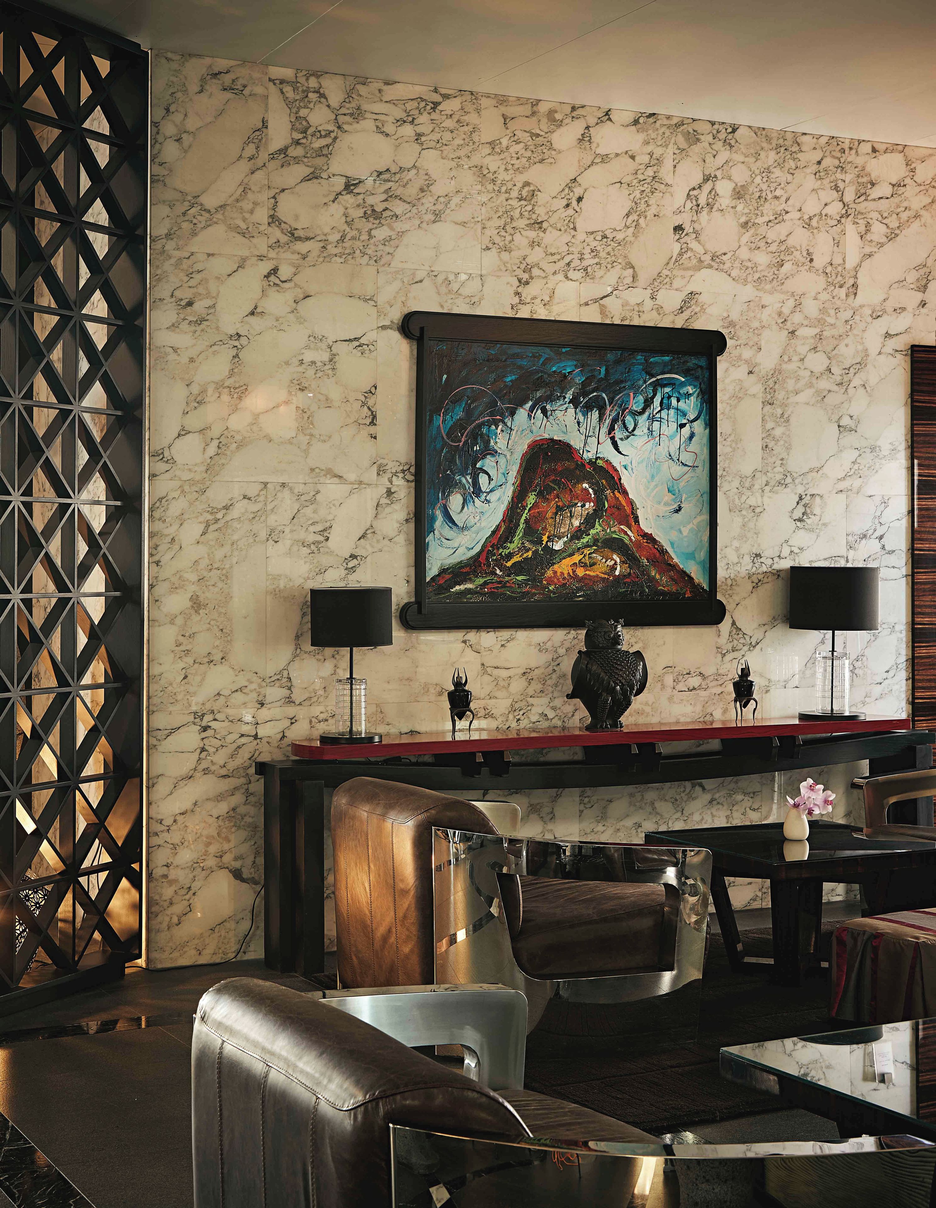Una habitación con pared de mármol, un cuadro abstracto enmarcado, una consola roja y muebles de cuero.