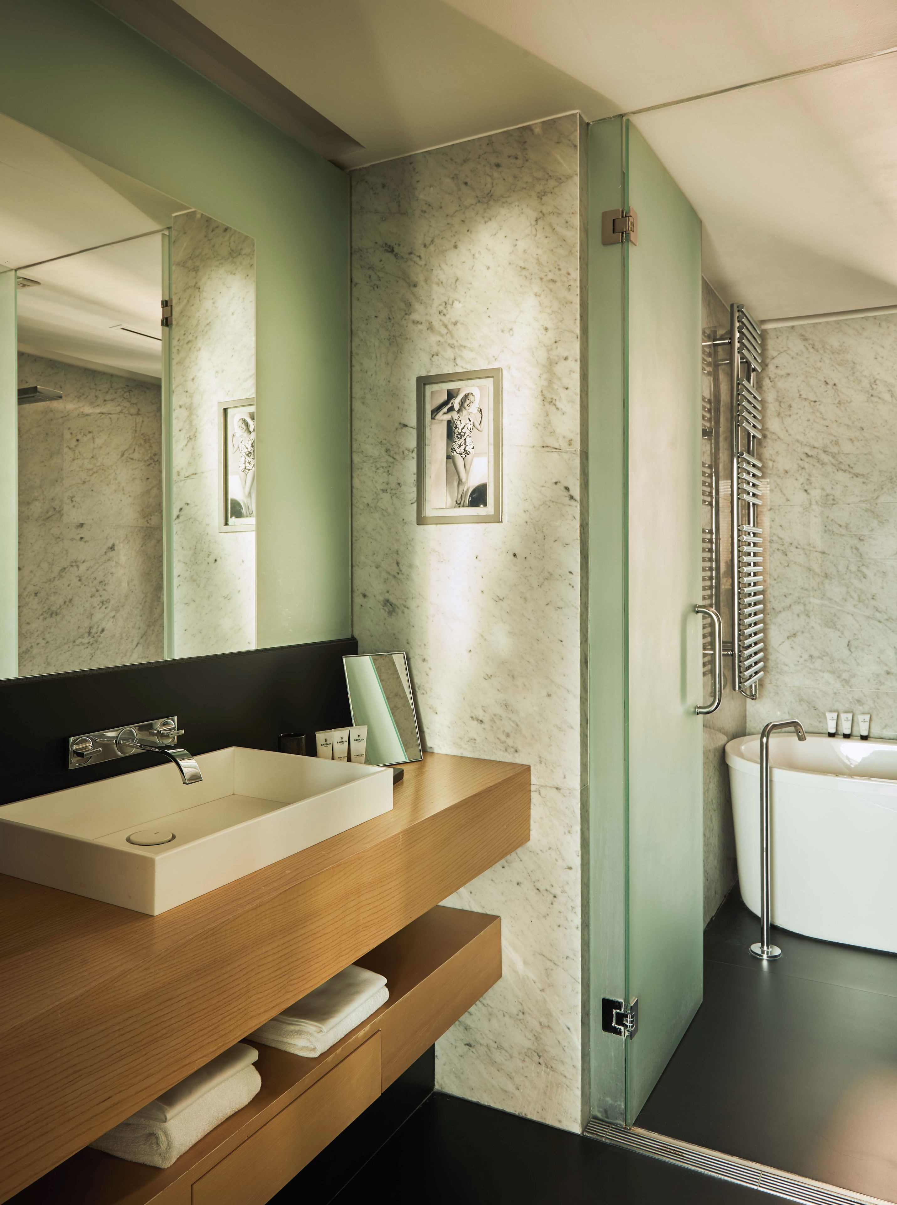 A modern bathroom with a large mirror, a sink, a bathtub, and a towel rack.