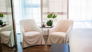 A hotel room with two beige armchairs, a small round table with a vase of white orchids, and a large mirror.