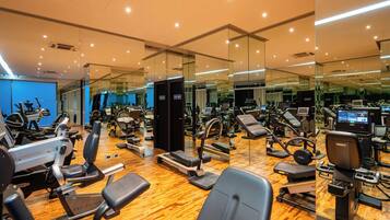 Un gimnasio con diverso equipamiento de ejercicio, paredes con espejos y suelo de madera.