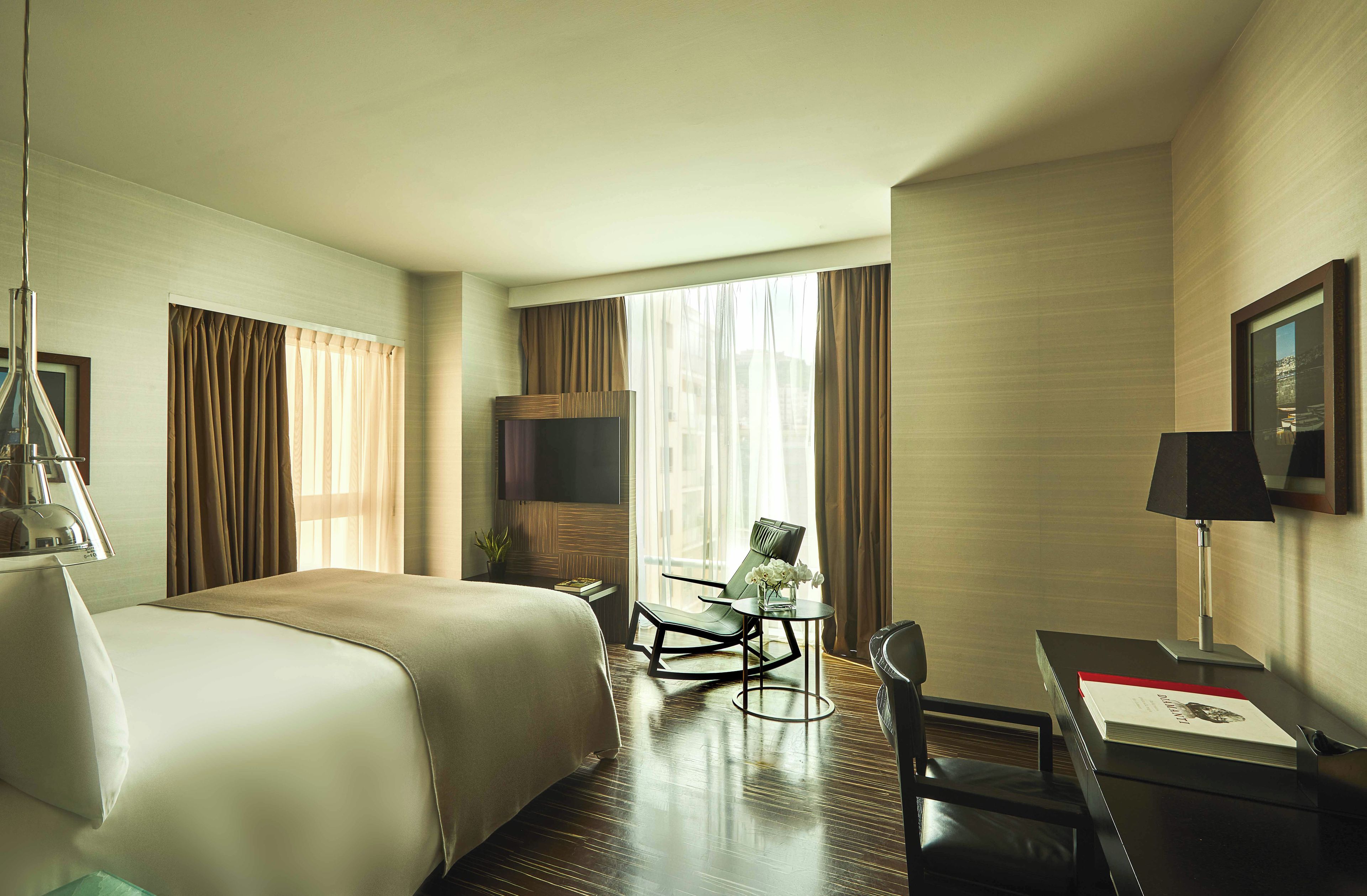 Une chambre d’hôtel avec un lit, un bureau, une chaise, une télévision et une fenêtre avec des rideaux.