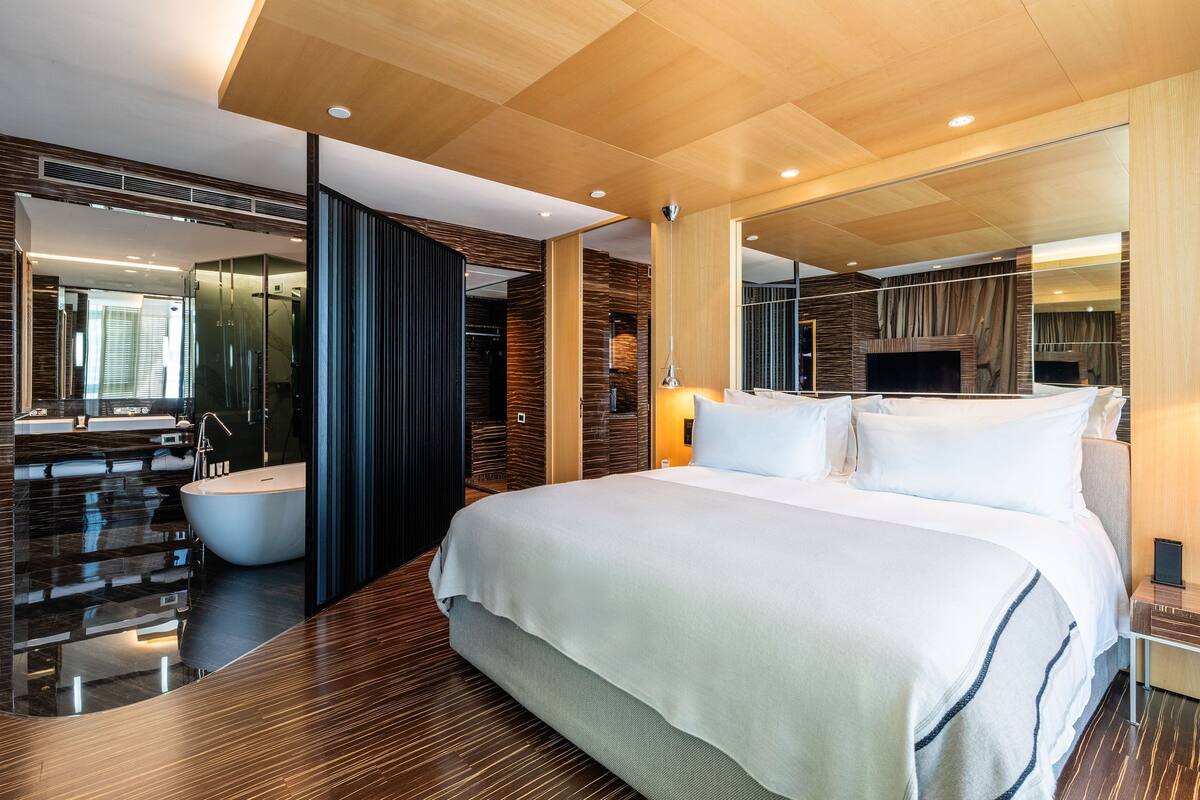 A modern hotel room with a large bed, a separate bathroom with a bathtub, and a large mirror.