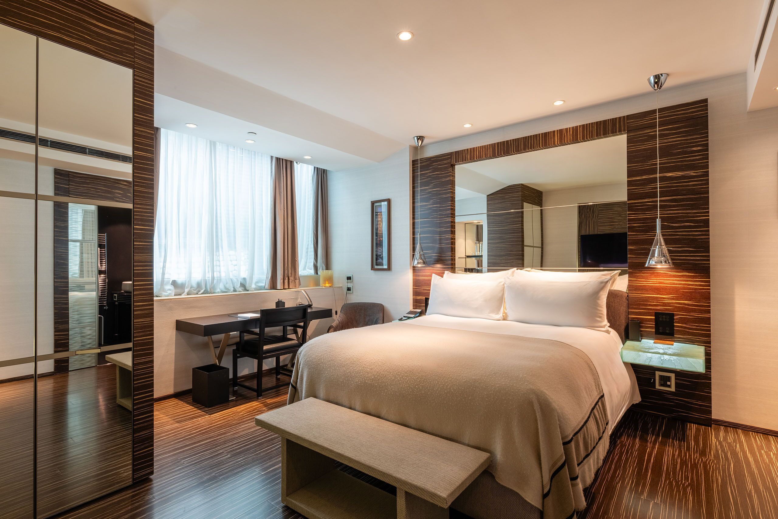 A modern hotel room with a large bed, a desk, and a mirror.