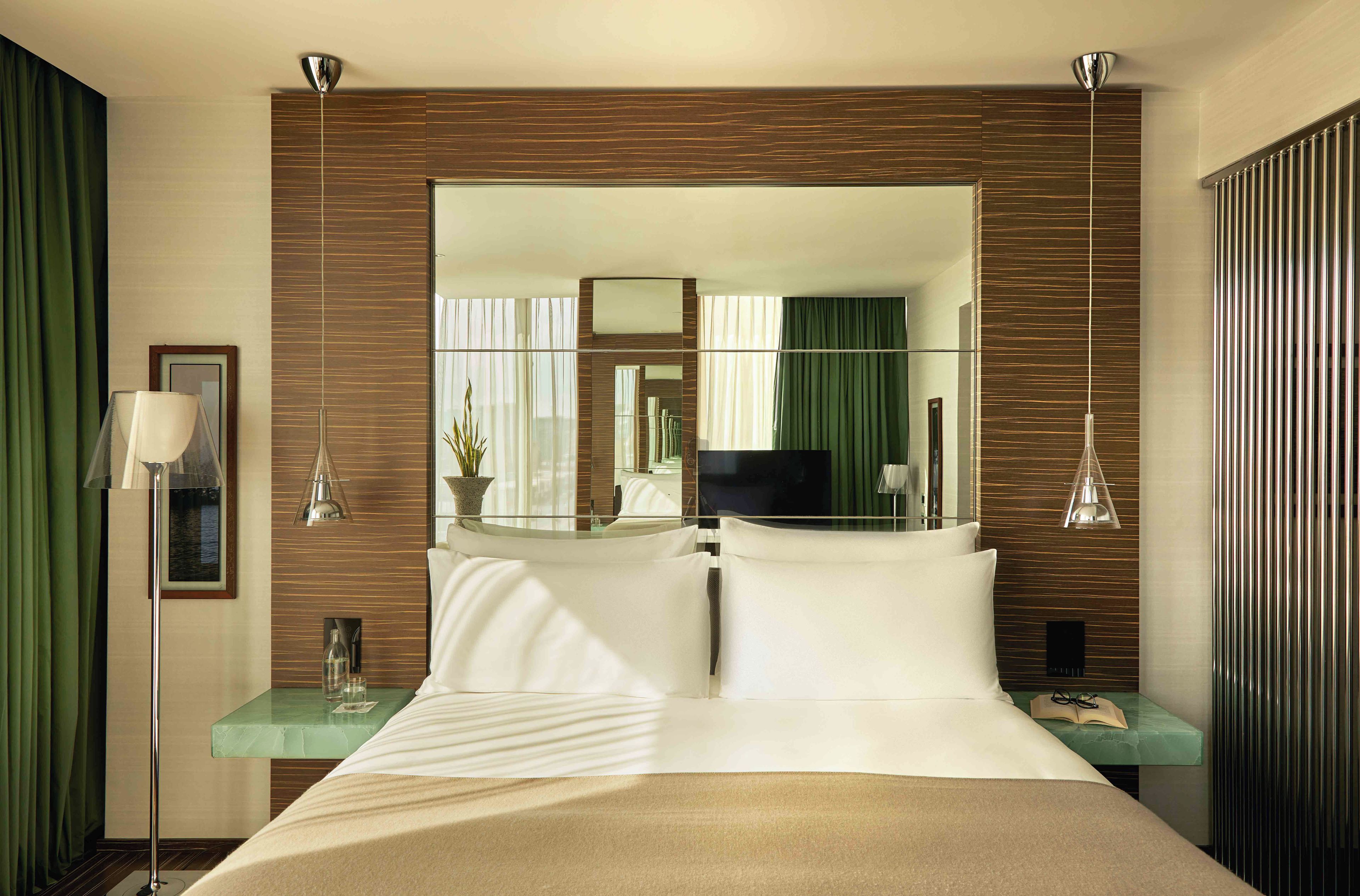 Une chambre d’hôtel avec un grand lit, un téléviseur à écran plat, un miroir et une table de chevet avec une lampe et un verre d’eau.