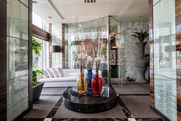 A modern lobby with a glass partition, a white sofa, and three vases with branches. - ROMEO Napoli (Naples)