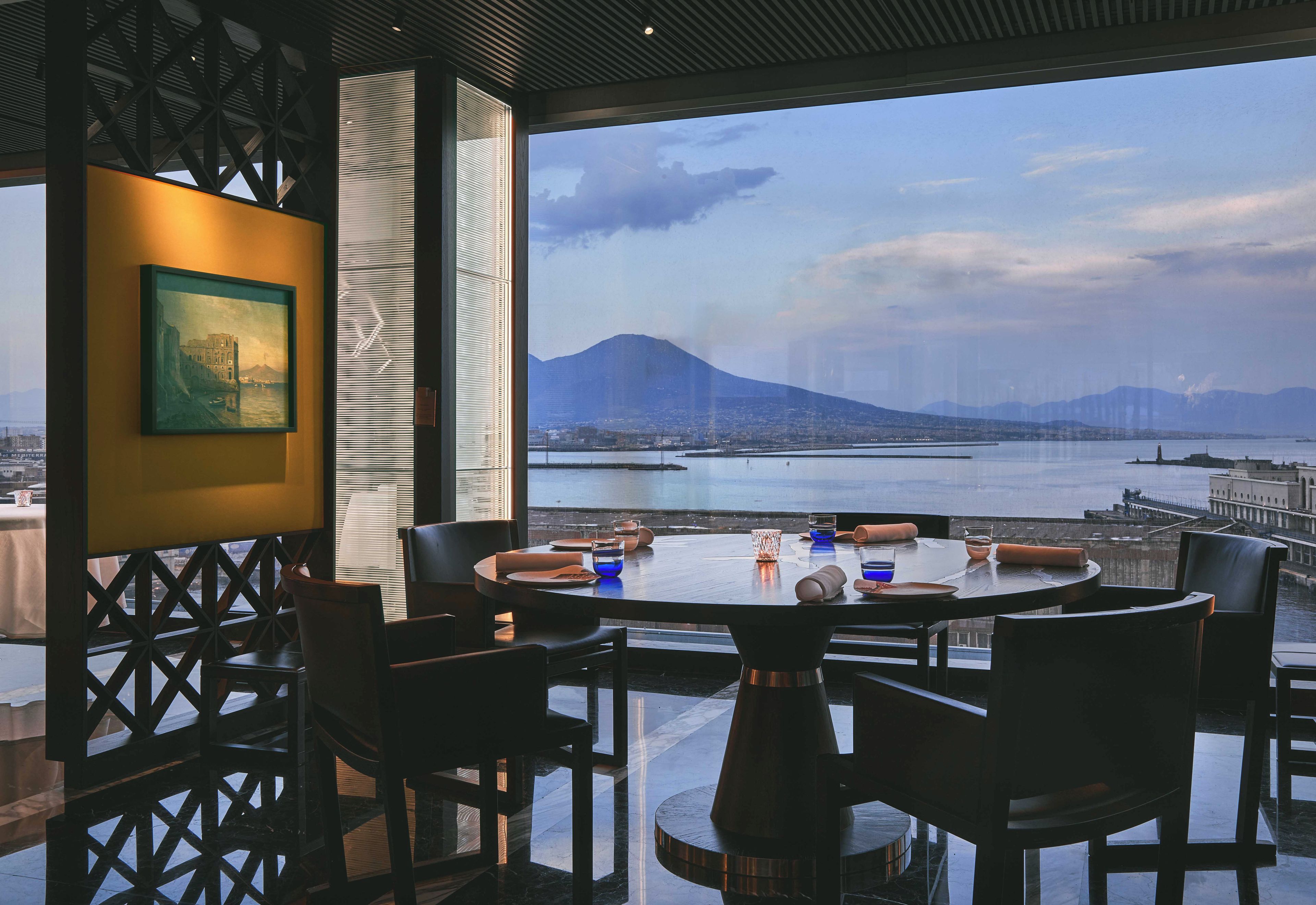 A dining area with a table set for four, overlooking a body of water and a mountain.