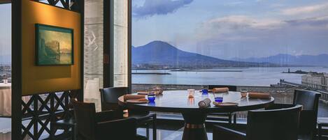 A dining area with a table set for four, overlooking a body of water and a mountain.