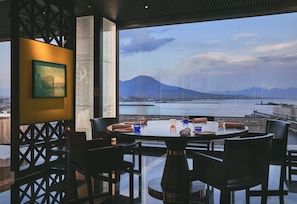 A dining area with a table set for four, overlooking a body of water and a mountain.