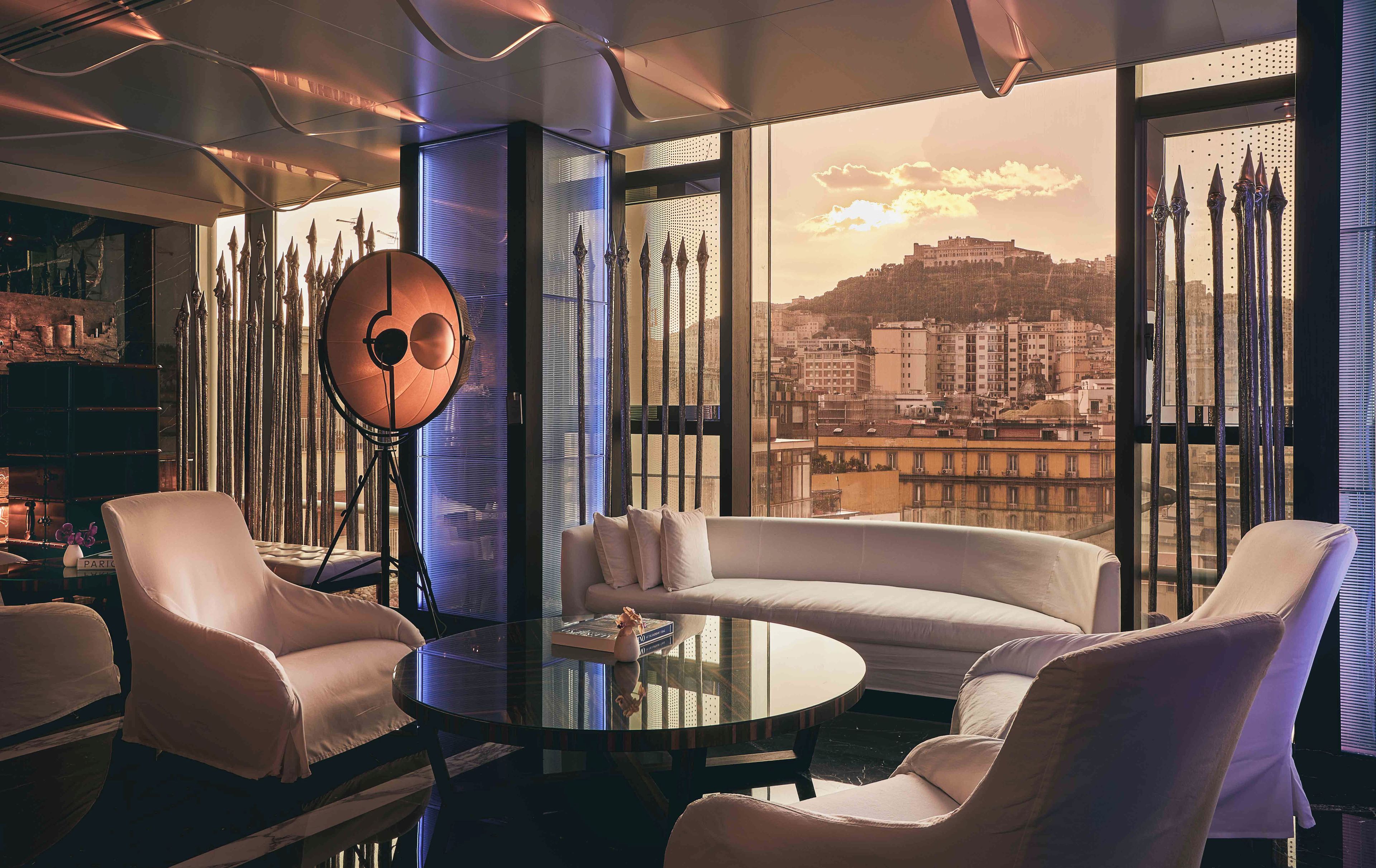 A modern interior with a round glass table, white sofas, and a large window with a city view.
