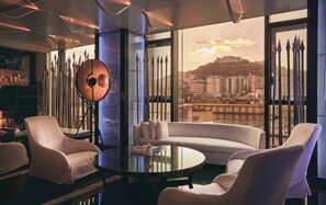 A modern interior with a round glass table, white sofas, and a large window with a city view.