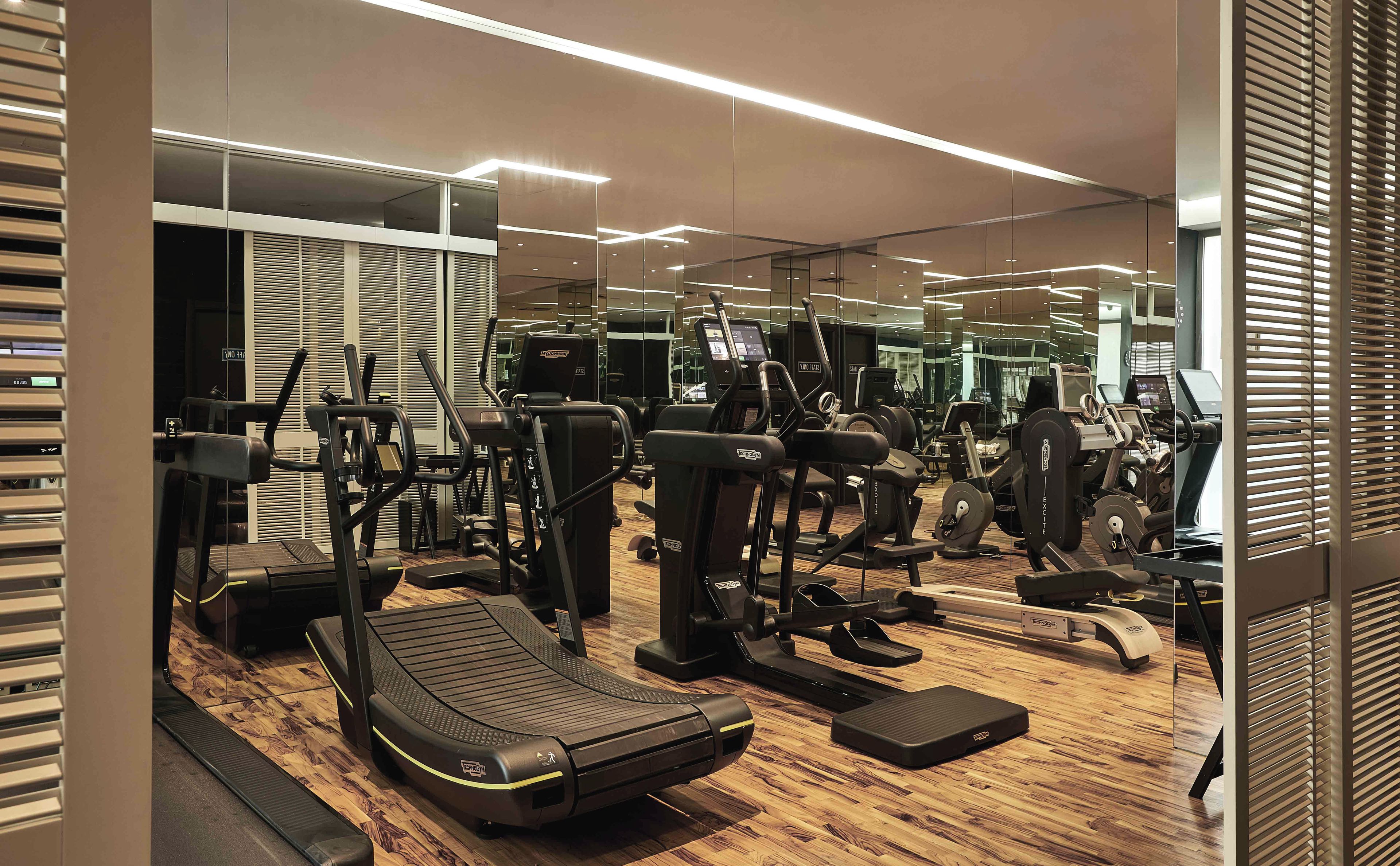 A modern gym with various exercise equipment, including treadmills and weight machines, and a wooden floor.