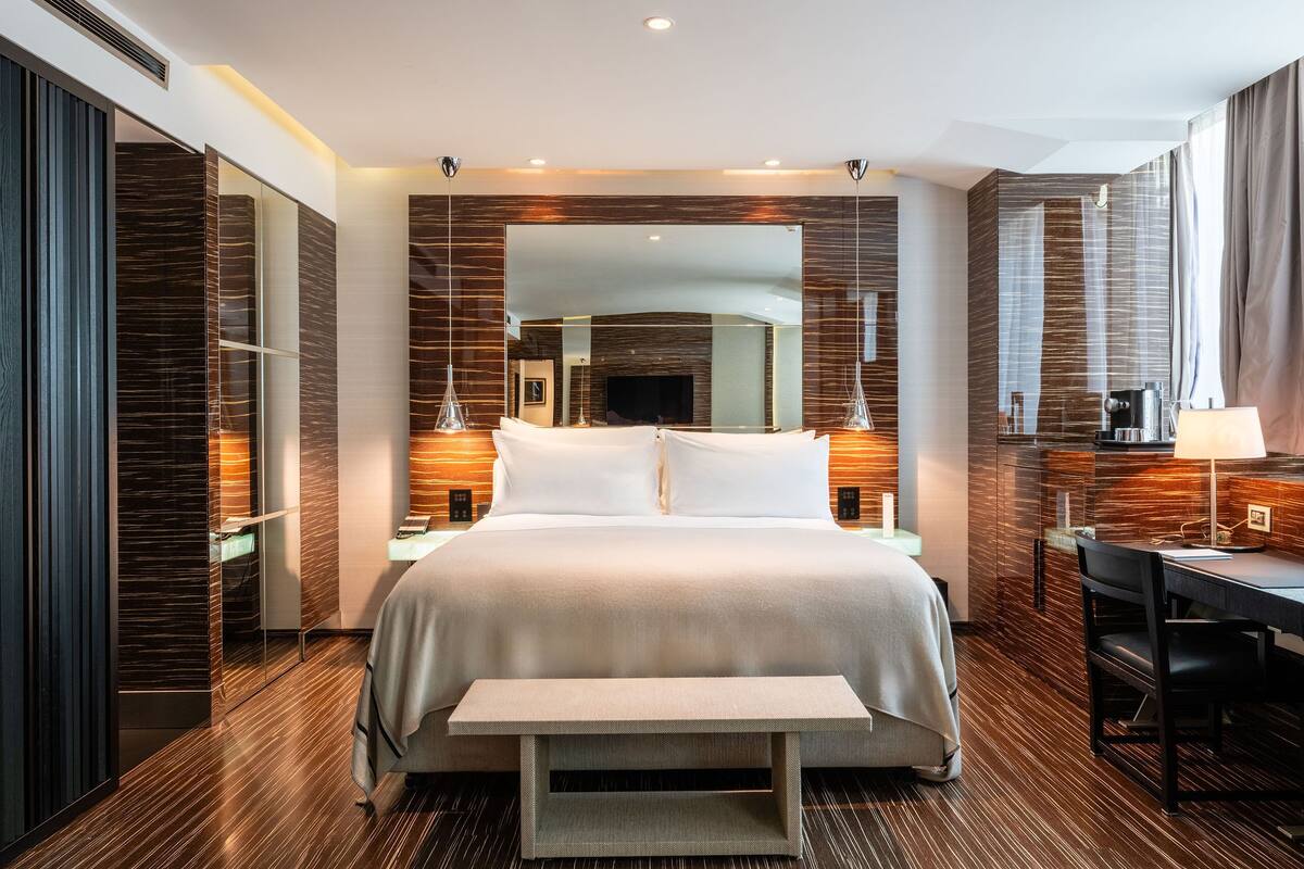 A modern hotel room with a large bed, bedside tables, a desk, and a bench.