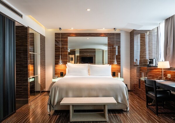 A modern hotel room with a large bed, bedside tables, a desk, and a bench.