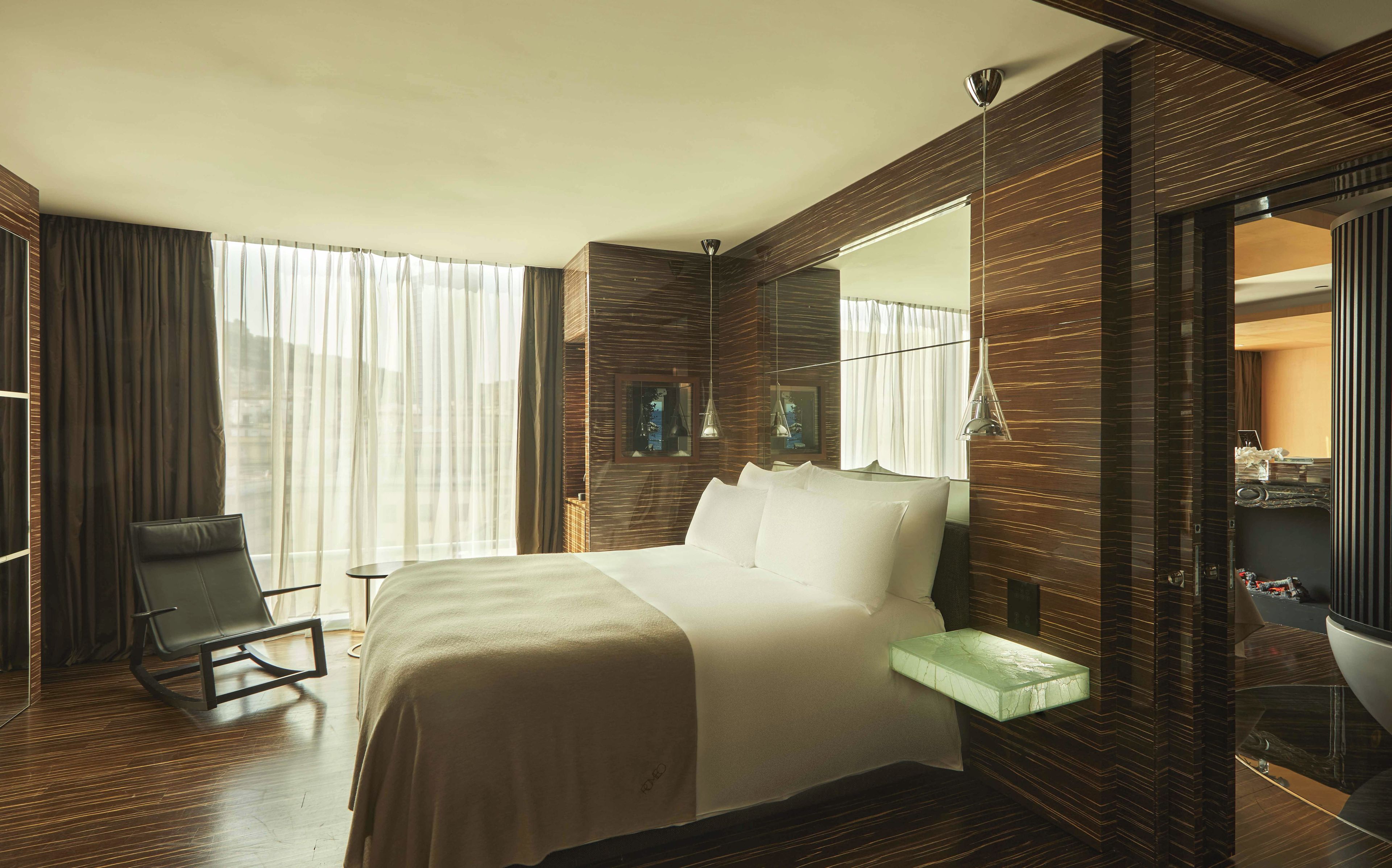 Une chambre d’hôtel avec un grand lit, une chaise, une table de chevet, un miroir et une vue sur la ville par la fenêtre.