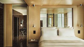 Una habitación de hotel moderna con una cama grande, una mesita de noche, un espejo y vistas a la ciudad desde la ventana.