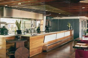 A modern restaurant interior with a wooden counter, seating area, and a view of the city through large windows.
