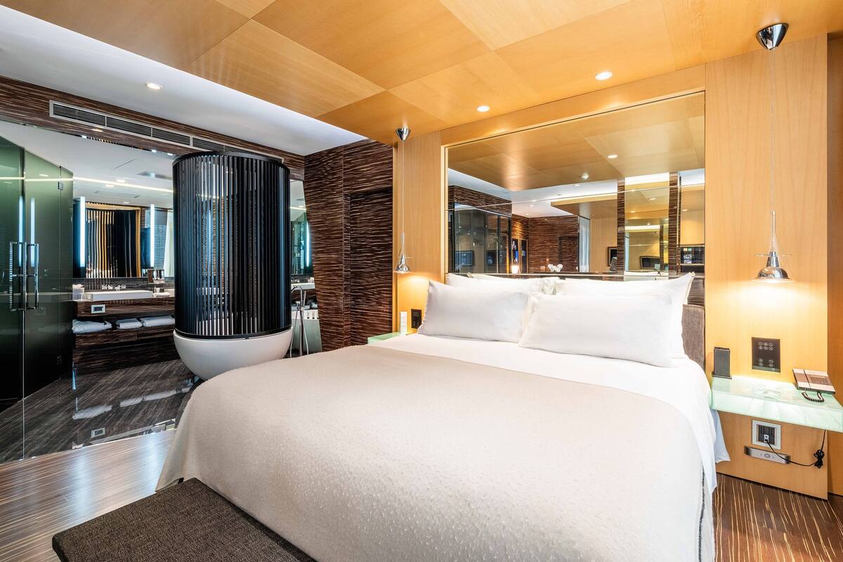 A modern hotel room with a large bed, a bathroom with a bathtub, and a large mirror.
