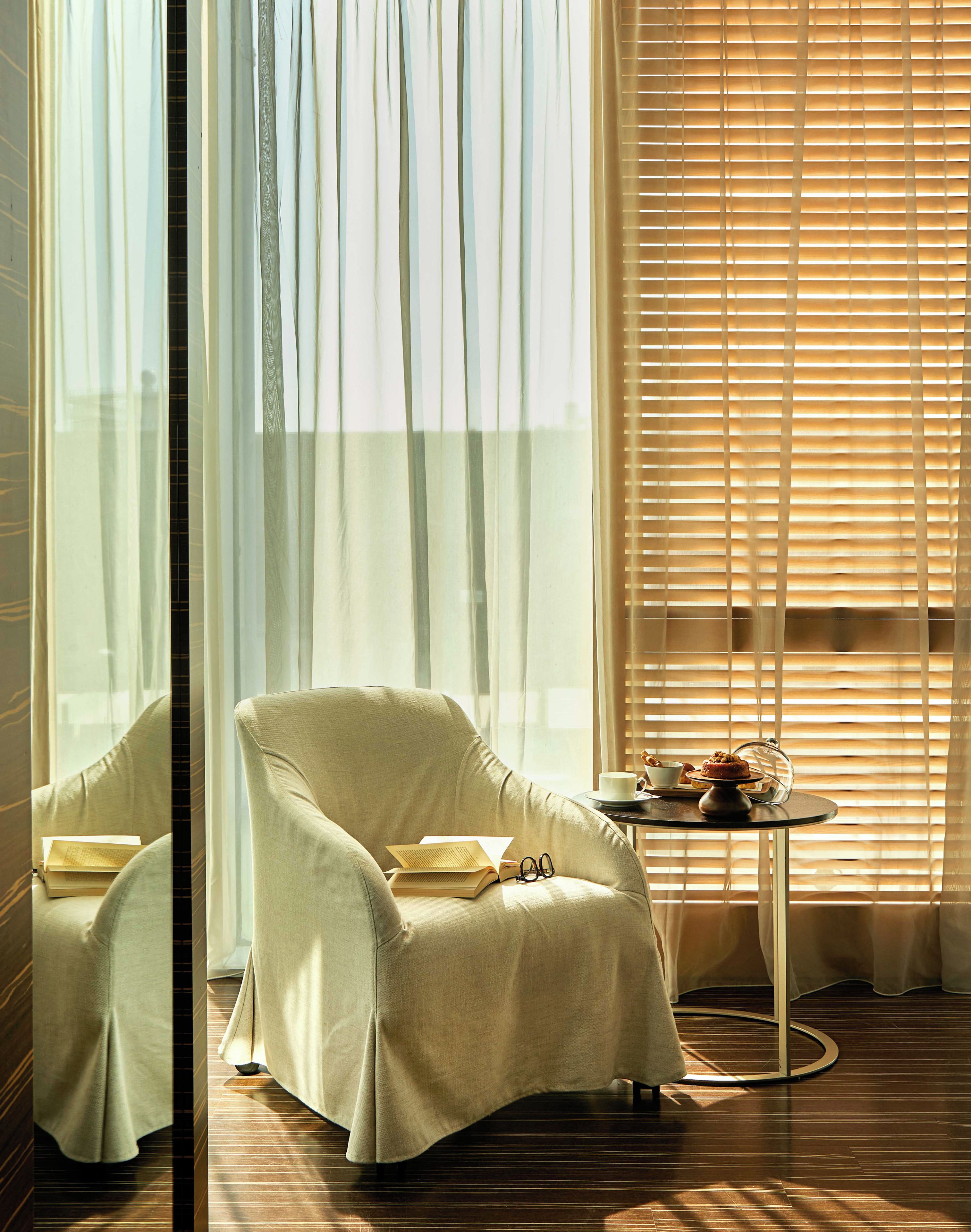 A room with a large window, a chair, a table with a cup and a plate, and a reflection of the window.