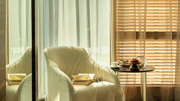 A room with a large window, a chair, a table with a cup and a plate, and a reflection of the window.
