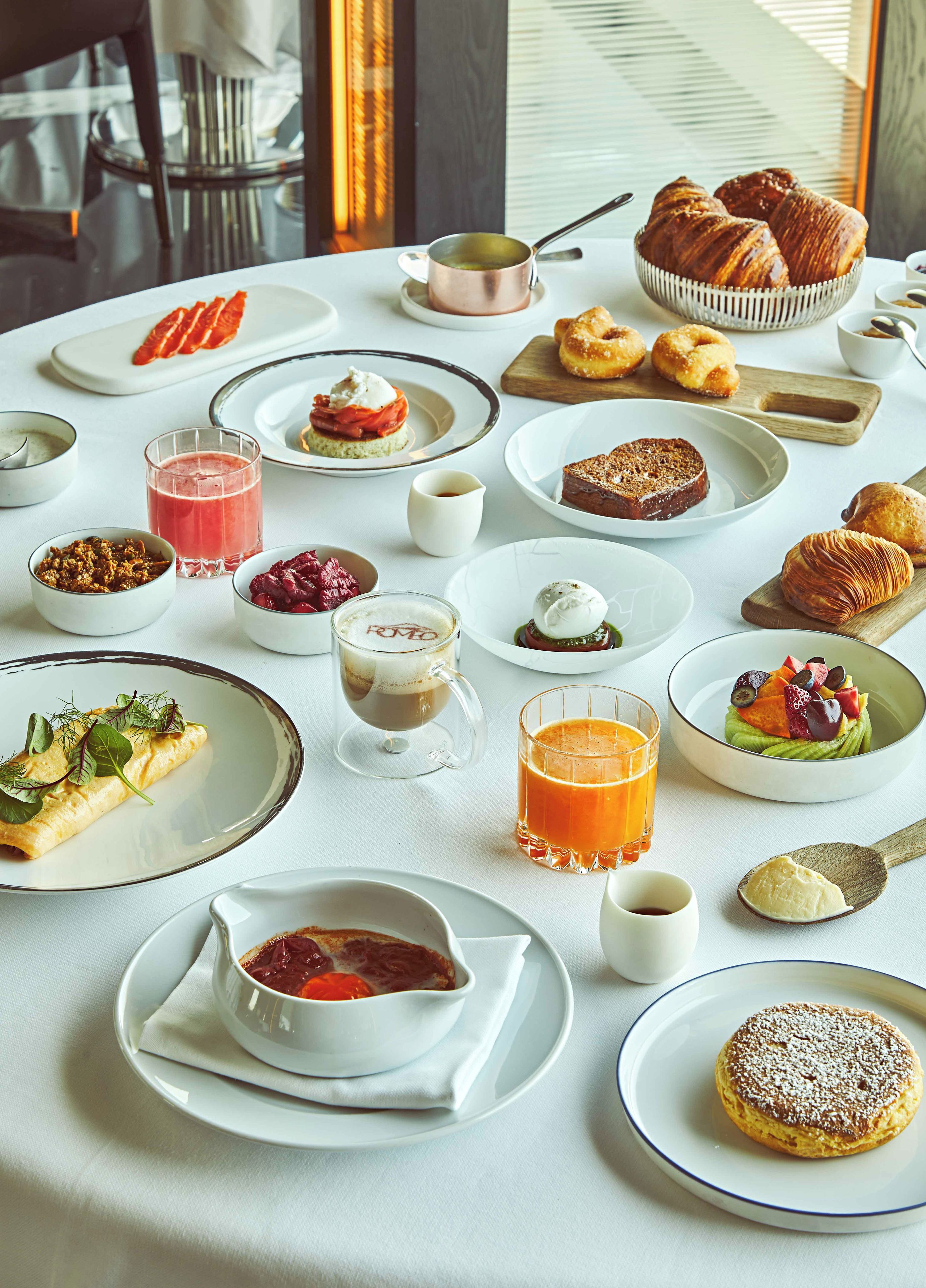 A breakfast setting with various dishes, drinks, and pastries on a table.