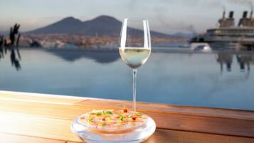 A clear glass of white wine on a wooden table with a view of a calm body of water and a cruise ship in the background.