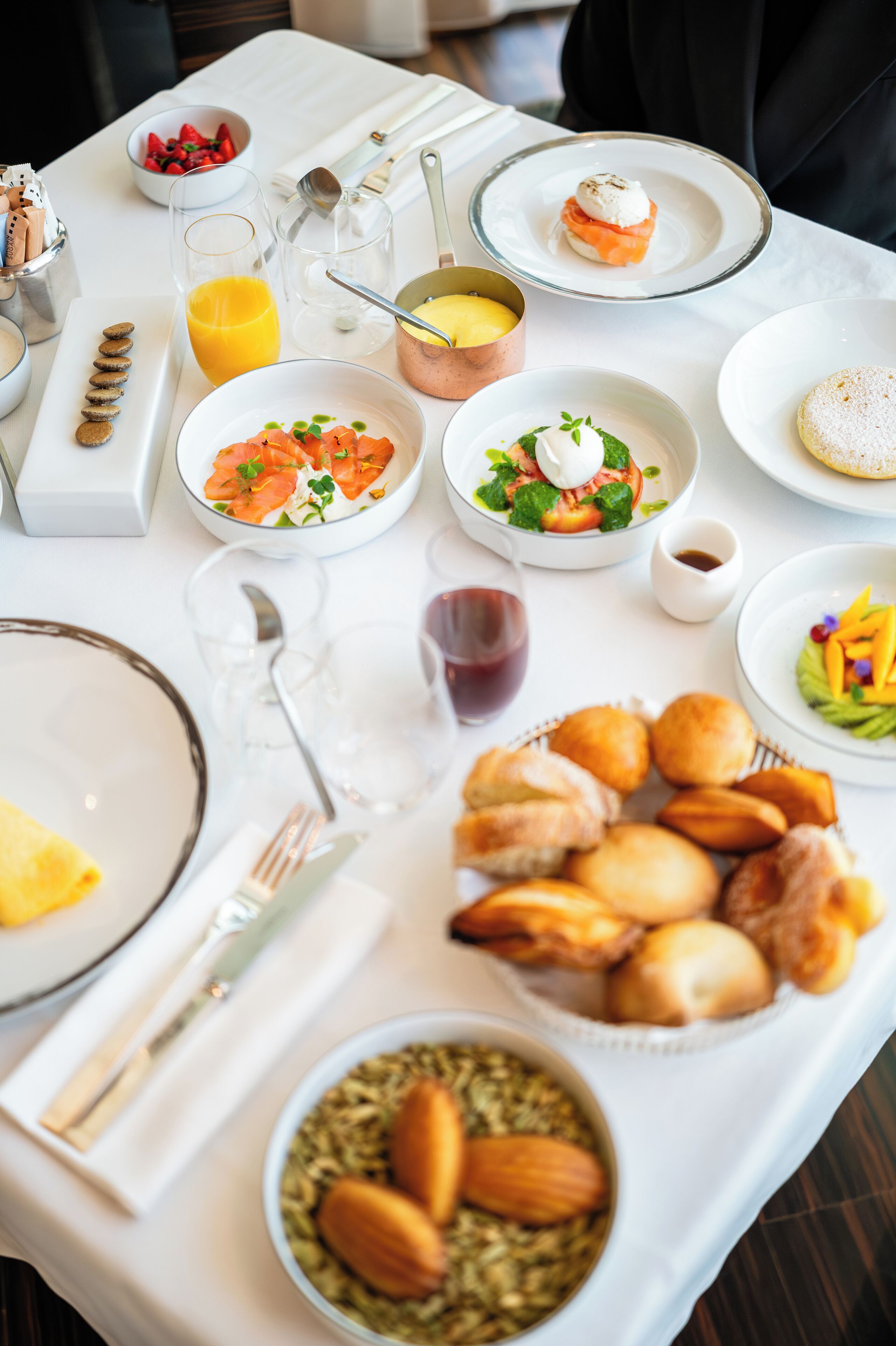 A breakfast table with various dishes, including a bowl of fruit, a plate of pastries, and a glass of orange juice.