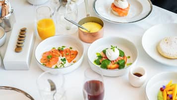 A breakfast table with various dishes, including a bowl of fruit, a plate of pastries, and a glass of orange juice.